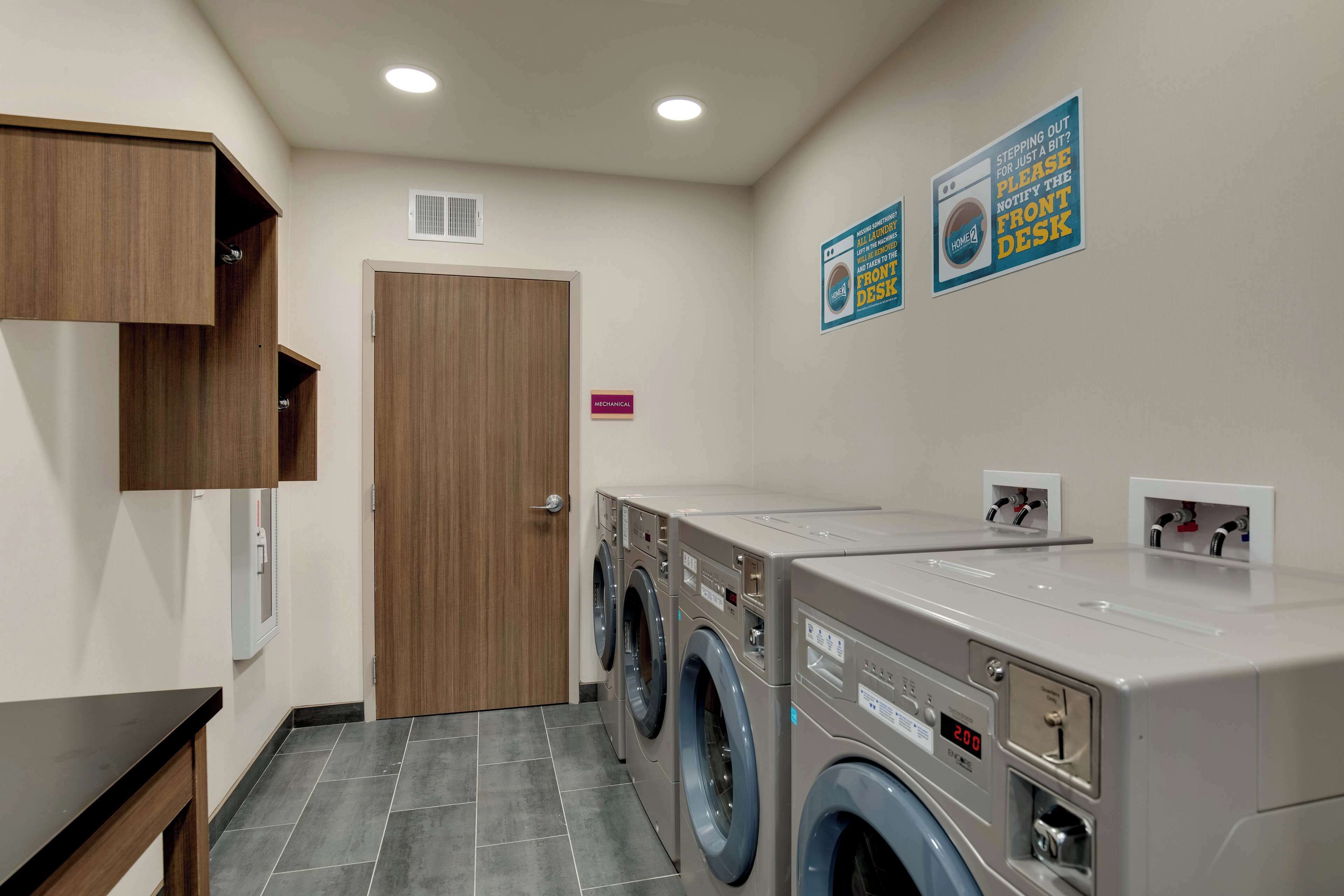 A laundry room with a wooden cabinet, a washing machine, and a dryer. There are signs on the wall and a door labeled "Mechanical."