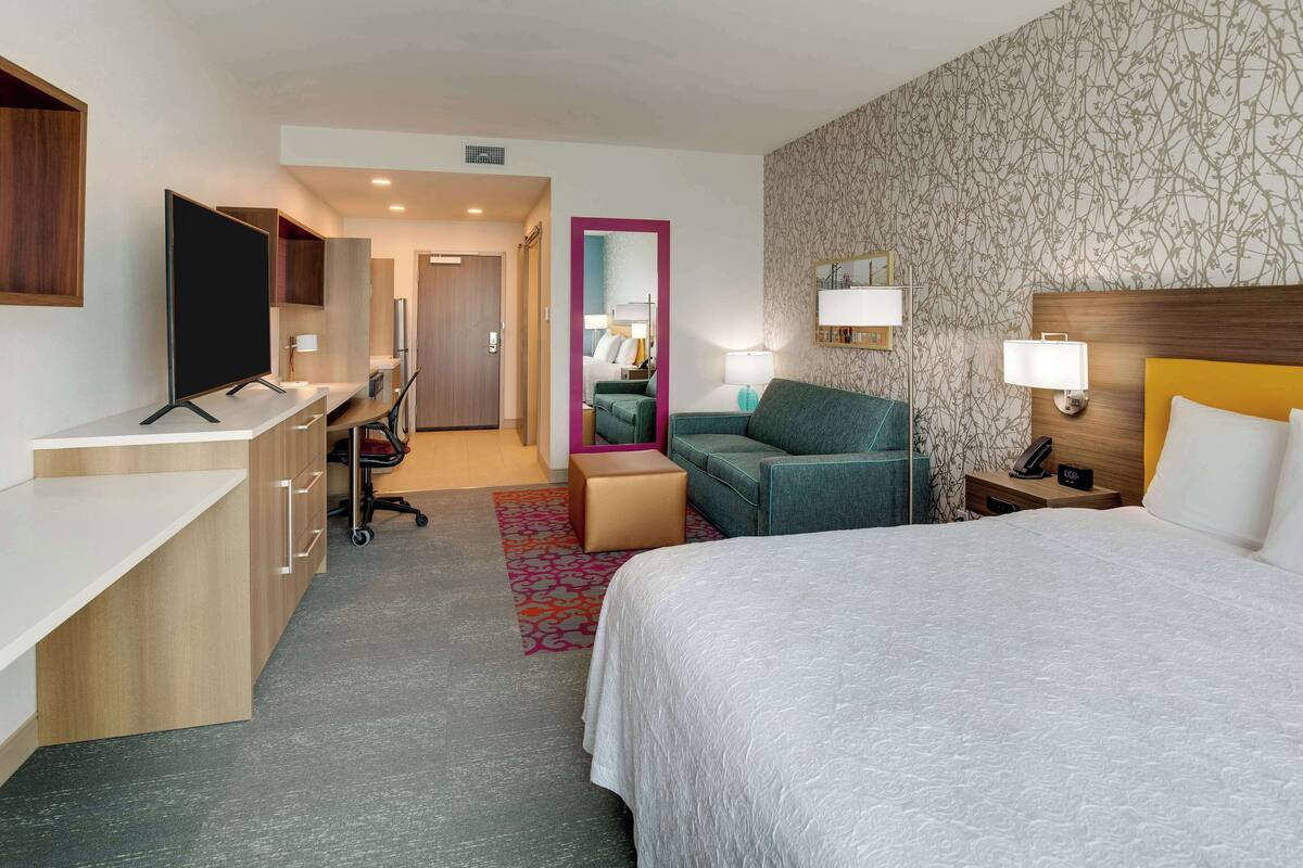 Quarto de hotel com cama, escrivaninha, cadeira e um pequeno espaço para sentar.