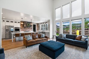 A spacious kitchen with modern appliances and a brick accent wall, a cozy seating area with a leather sofa and ottoman, and large windows offering a view of the outdoors.