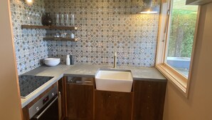 Une cuisine compacte avec un crédence à motifs, un four encastré et une fenêtre donnant sur un espace verdoyant.