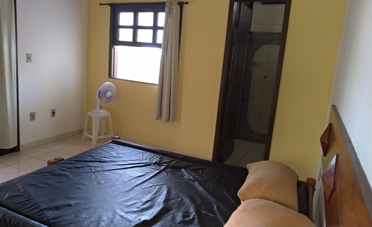 A room with a bed, a standing fan, a window with curtains, and a shower area.