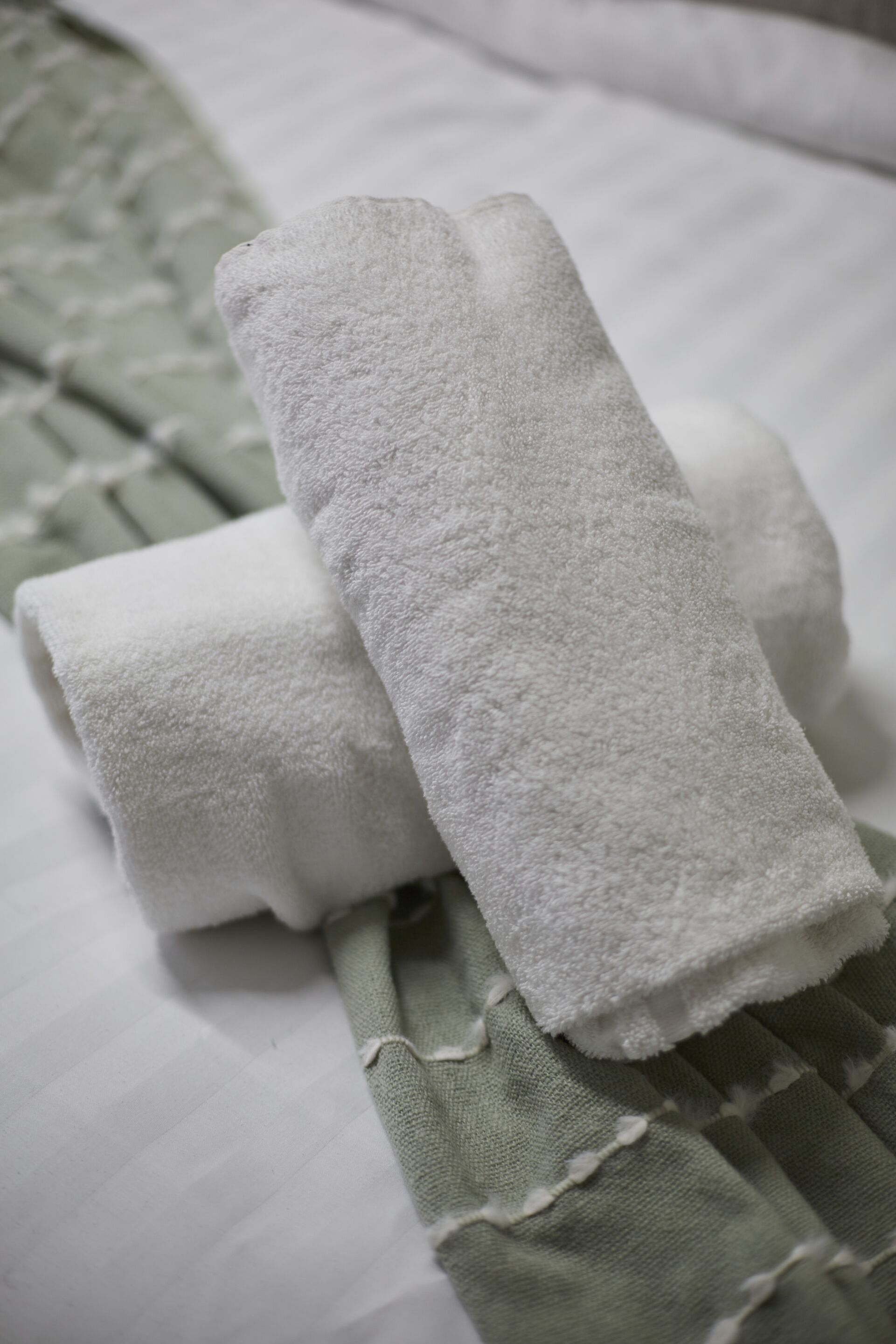 A neatly folded white towel on a bed with a green and white striped bedspread.