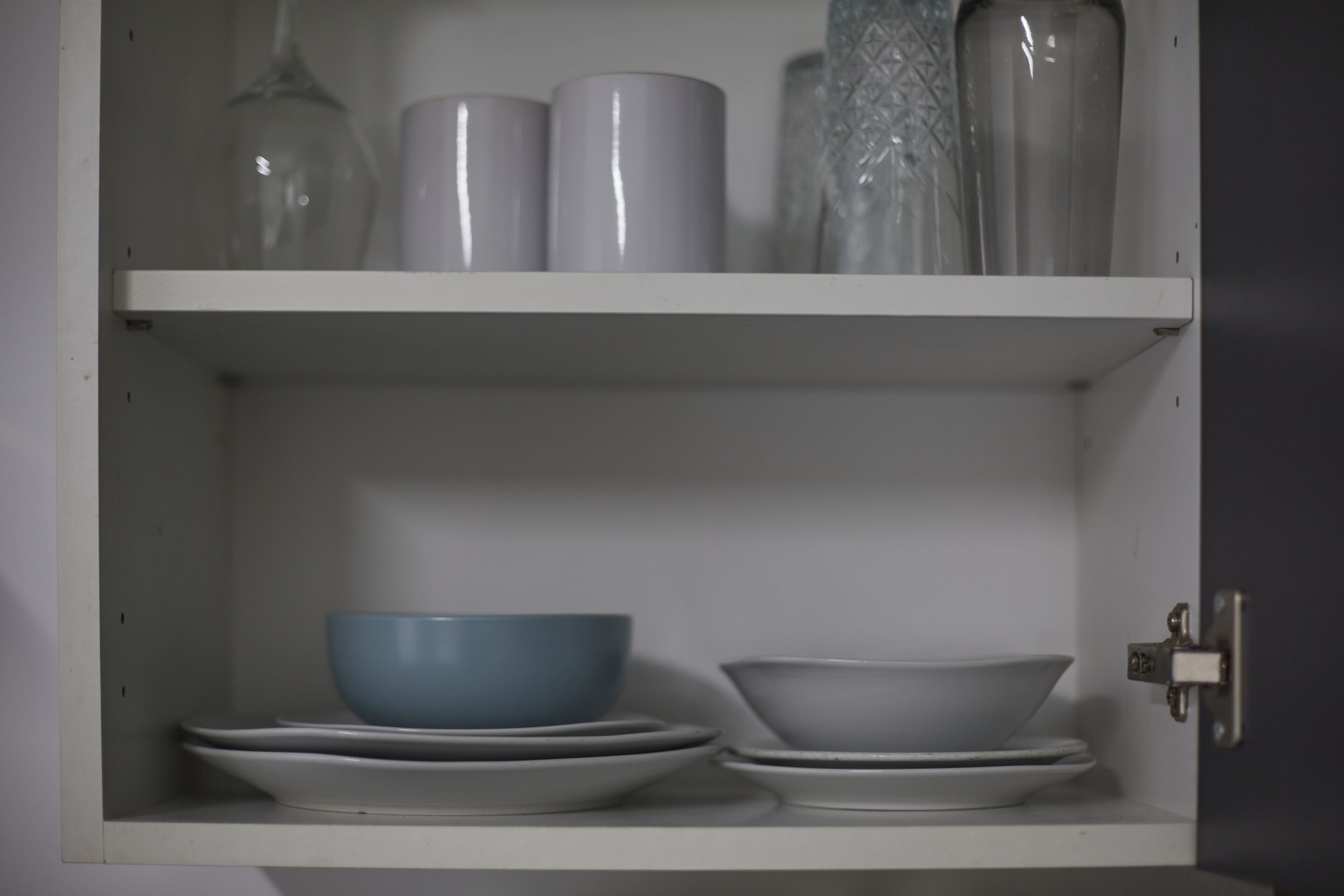 A white cabinet with shelves containing bowls, plates, and glassware.