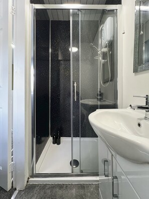 A modern bathroom with a glass-enclosed shower, a white sink, and a mirror above the sink. - Hayy Vibrant Studios Queensgate (Huddersfield)