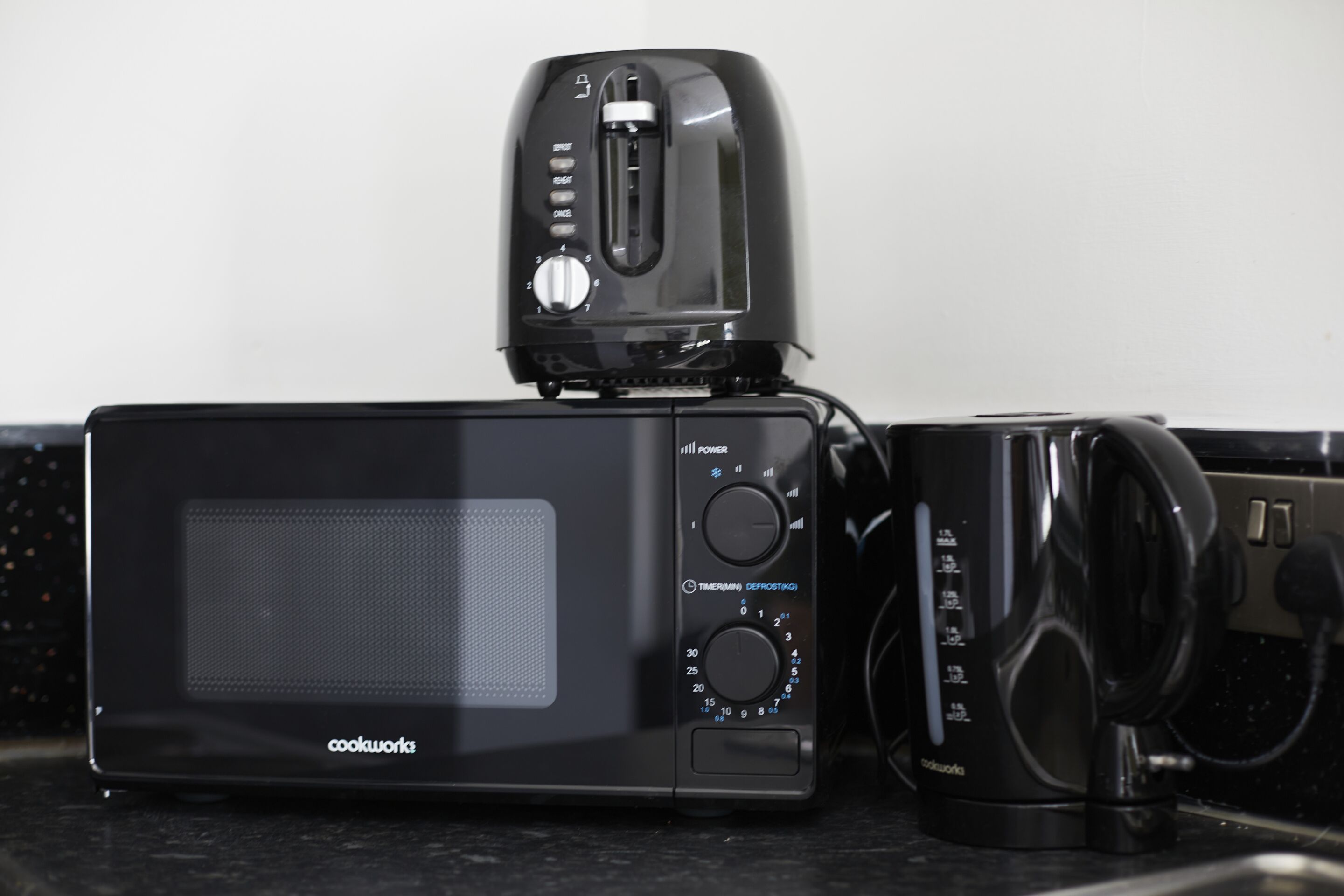 A black Cookware microwave oven with a toaster on top, placed on a dark countertop.