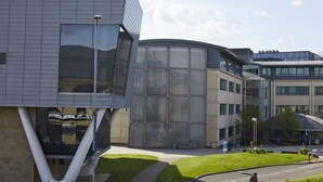 A modern building with a curved glass facade, a grassy courtyard, and a clear sky. - Hayy Vibrant Studios Queensgate (Huddersfield)