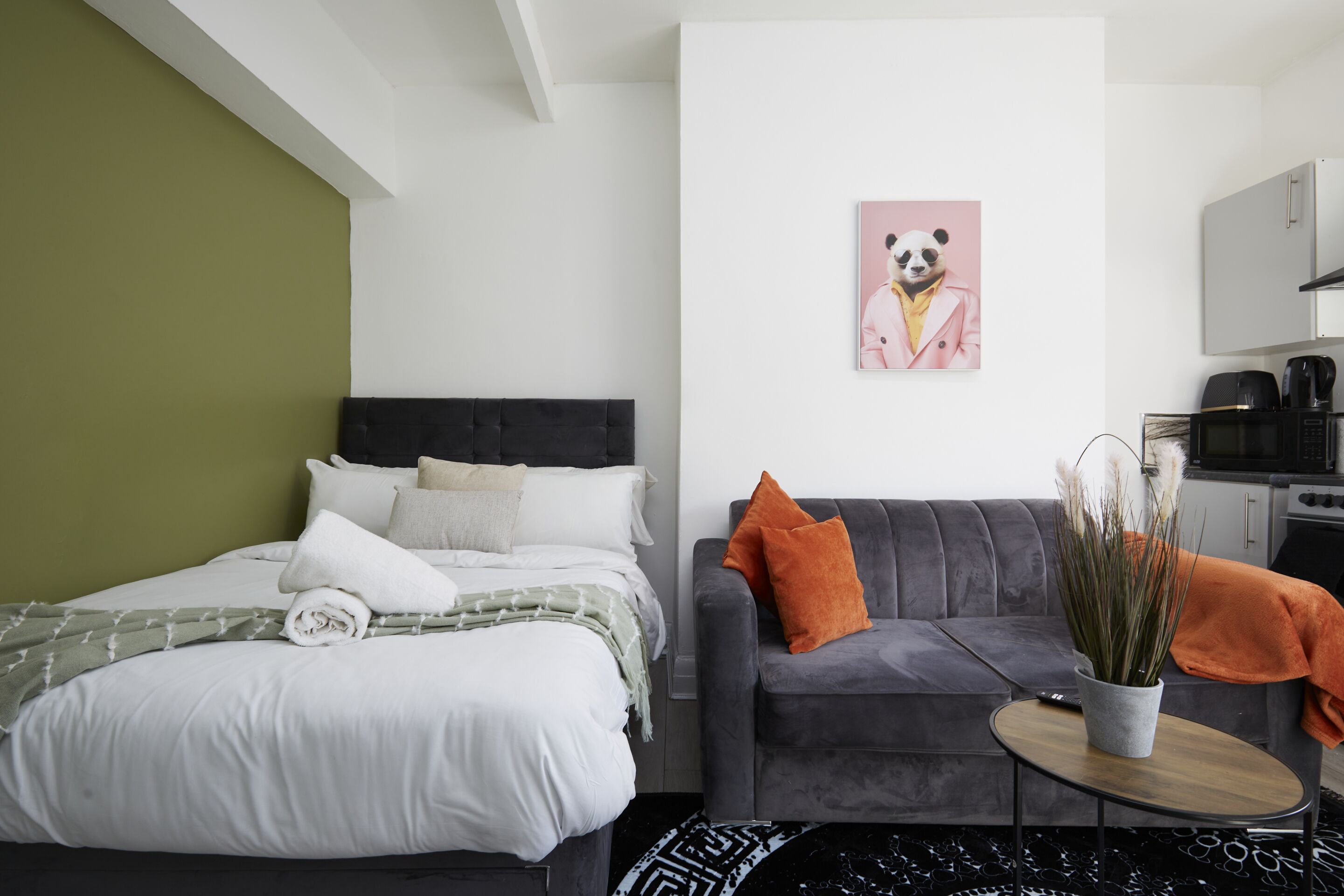 Een moderne slaapkamer met een bed, een grijze bank en een kleine tafel met een plant.
