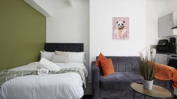 Een moderne slaapkamer met een bed, een grijze bank en een kleine tafel met een plant.