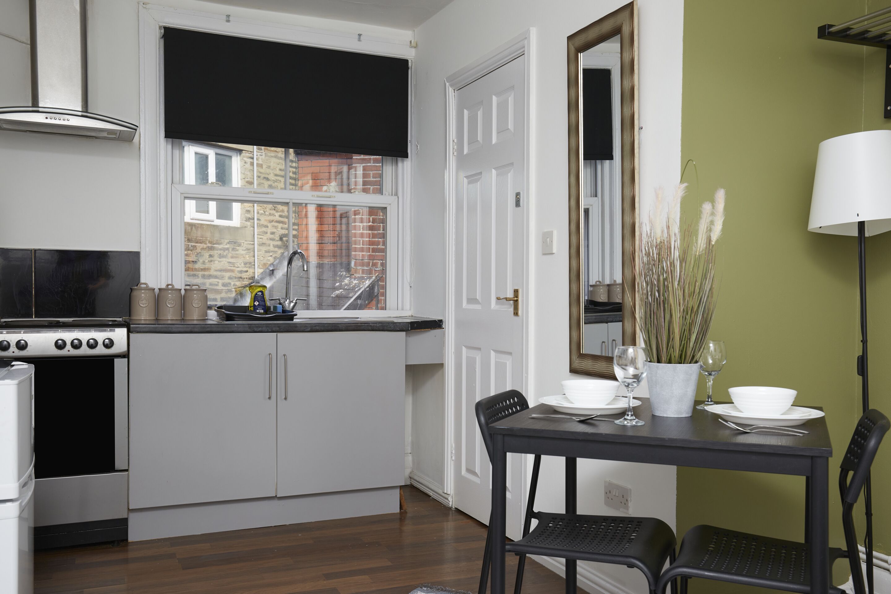 A kitchen with white cabinets, a stove, and a window with a black blind.