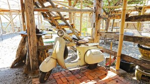 Een klassieke witte scooter staat geparkeerd onder een houten constructie met een metselwerk vloer.