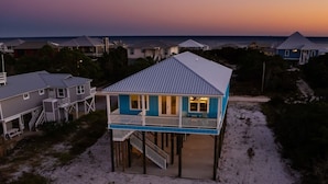 Uma casa à beira-mar com dois andares, varanda, terraço coberto e escada que leva ao andar superior.