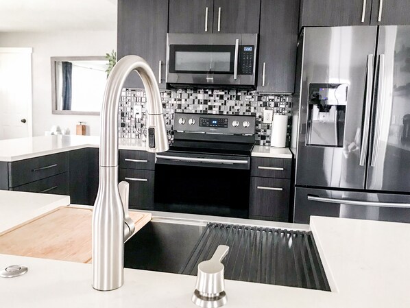 Una cocina moderna con electrodomésticos de acero inoxidable, un salpicadero de azulejos negros y un grifo elegante.