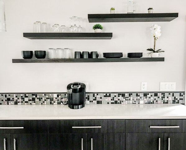 Una cocina moderna con gabinetes negros, una cafetera y varias estanterías con cristalería y plantas.
