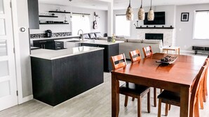 Una cocina moderna con una isla central, un comedor con sillas de madera y una chimenea.