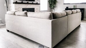 Una sala de estar moderna con un sofá seccional beige grande, un televisor de pantalla plana montado sobre una chimenea y un ventanal que proporciona luz natural.