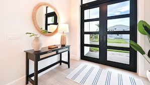 A modern entryway with a black-framed window, a console table with a mirror and lamp, and a potted plant. - Hot Tub & Heated Pool, 8 Bikes, 2 King Beds and Suites! (Marco Island)