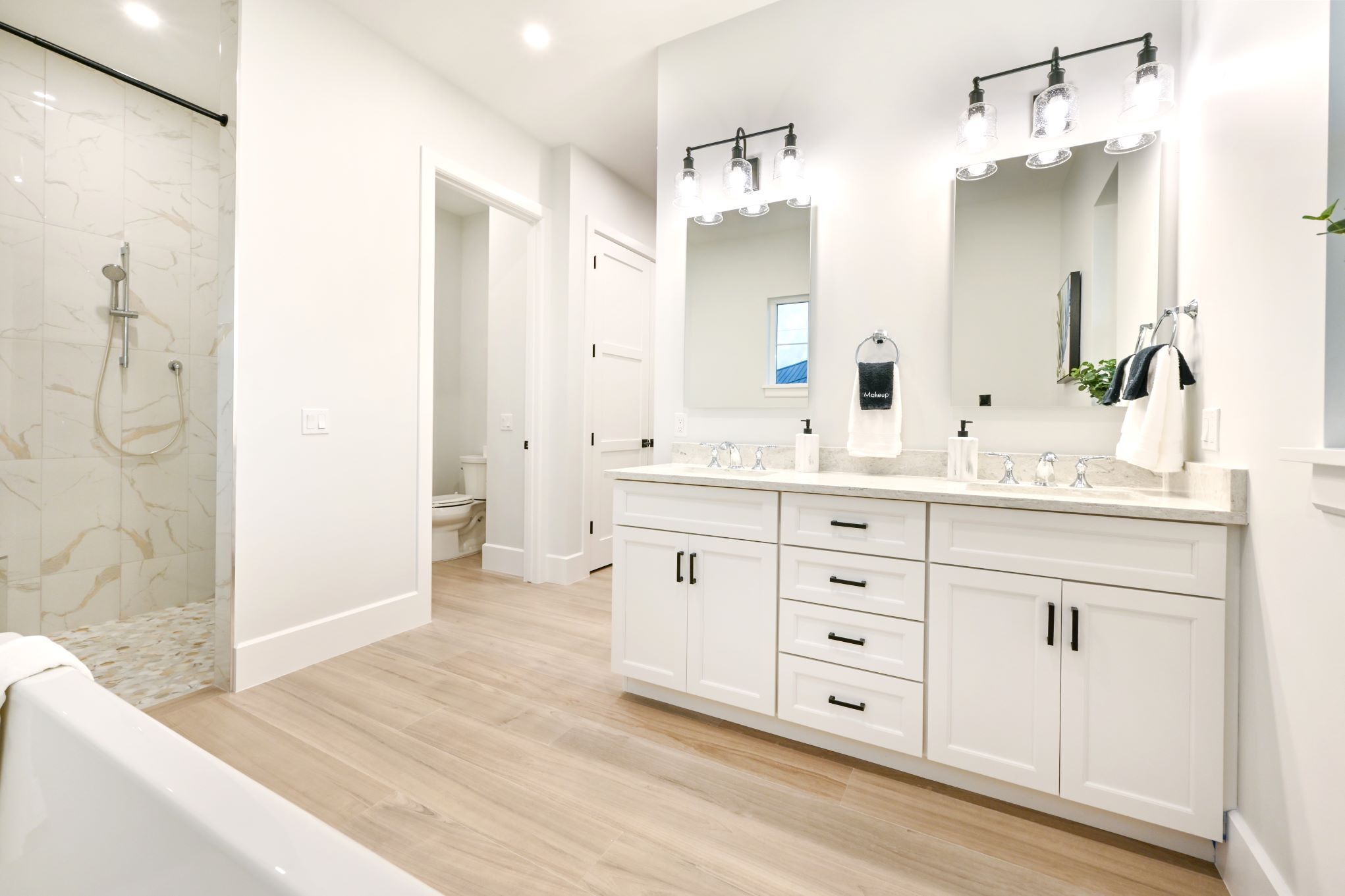 A modern bathroom with a large vanity, a walk-in shower, and a mirror with lights.