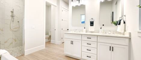 A modern bathroom with a large vanity, a walk-in shower, and a mirror with lights.