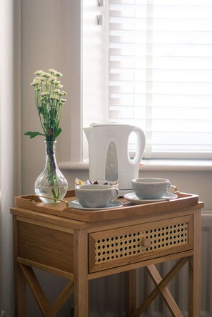 A wooden table with a glass vase of flowers, a white electric kettle, and a set of white cups and saucers.