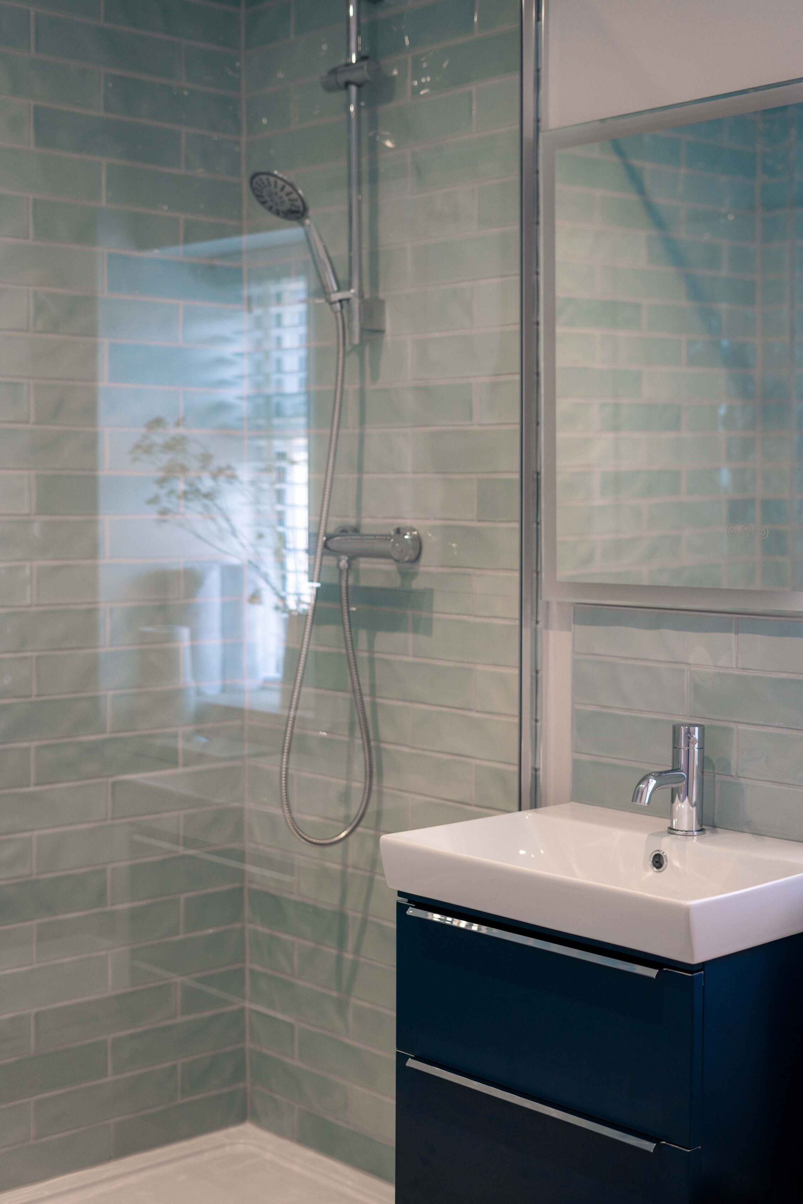 A bathroom with a glass shower enclosure, a white sink, and a blue cabinet.