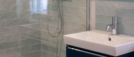 A bathroom with a glass shower enclosure, a white sink, and a blue cabinet.