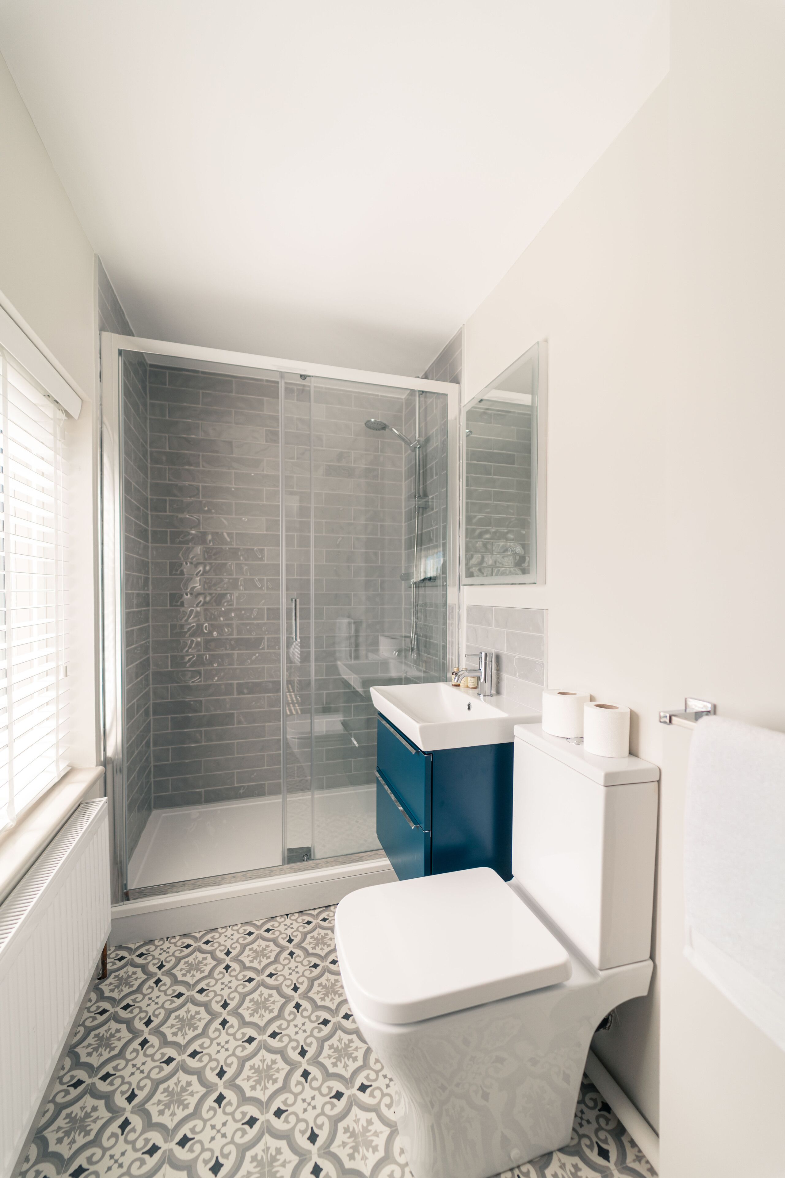 Un baño moderno con ducha envuelta en vidrio, inodoro blanco y tocador azul.