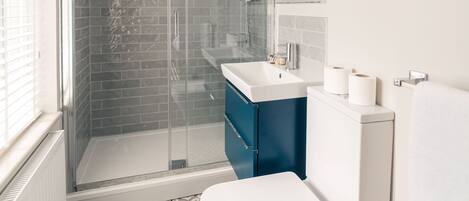 Un baño moderno con ducha envuelta en vidrio, inodoro blanco y tocador azul.