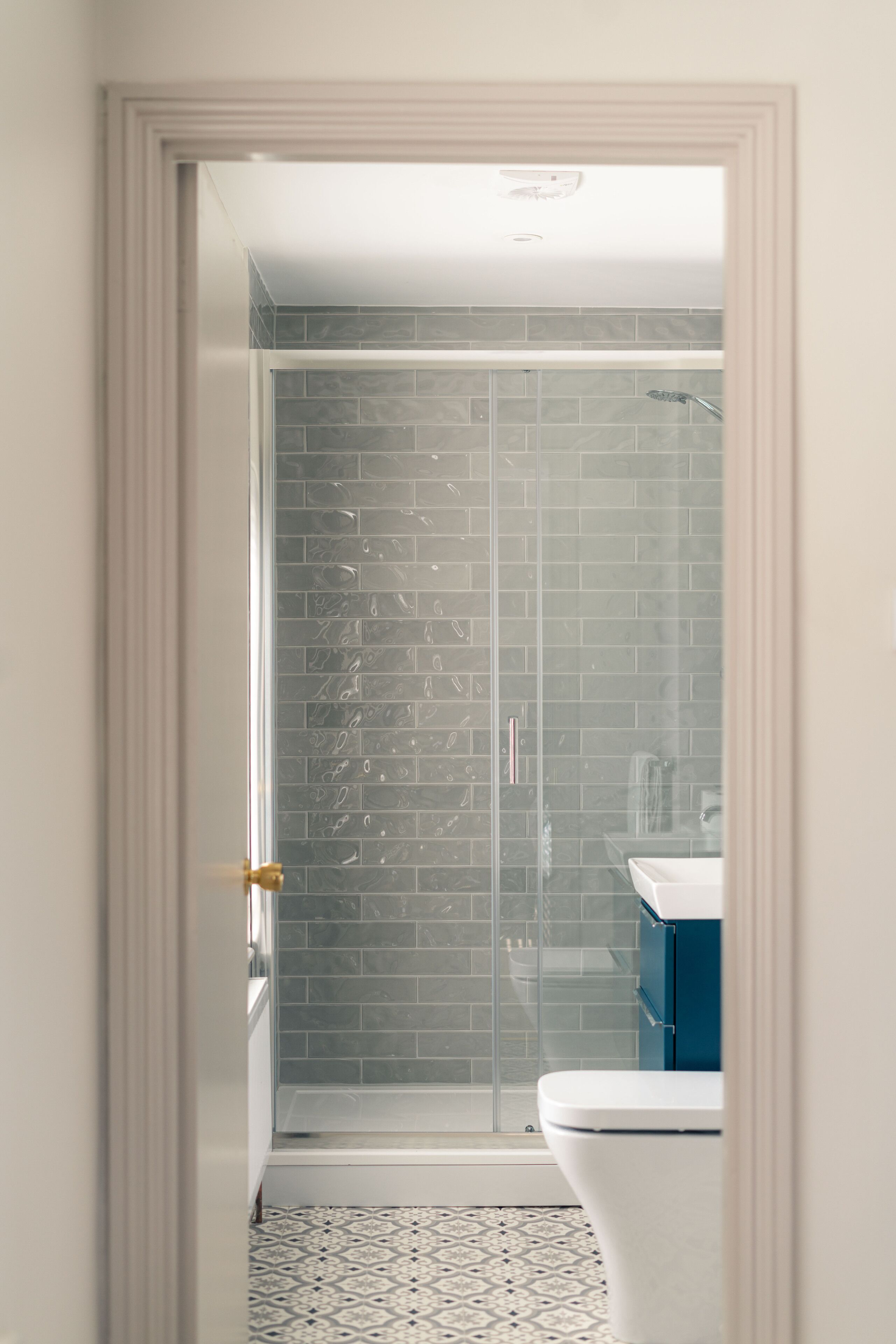 Une salle de bain avec une douche à parois de verre, des toilettes blanches et un meuble bleu.