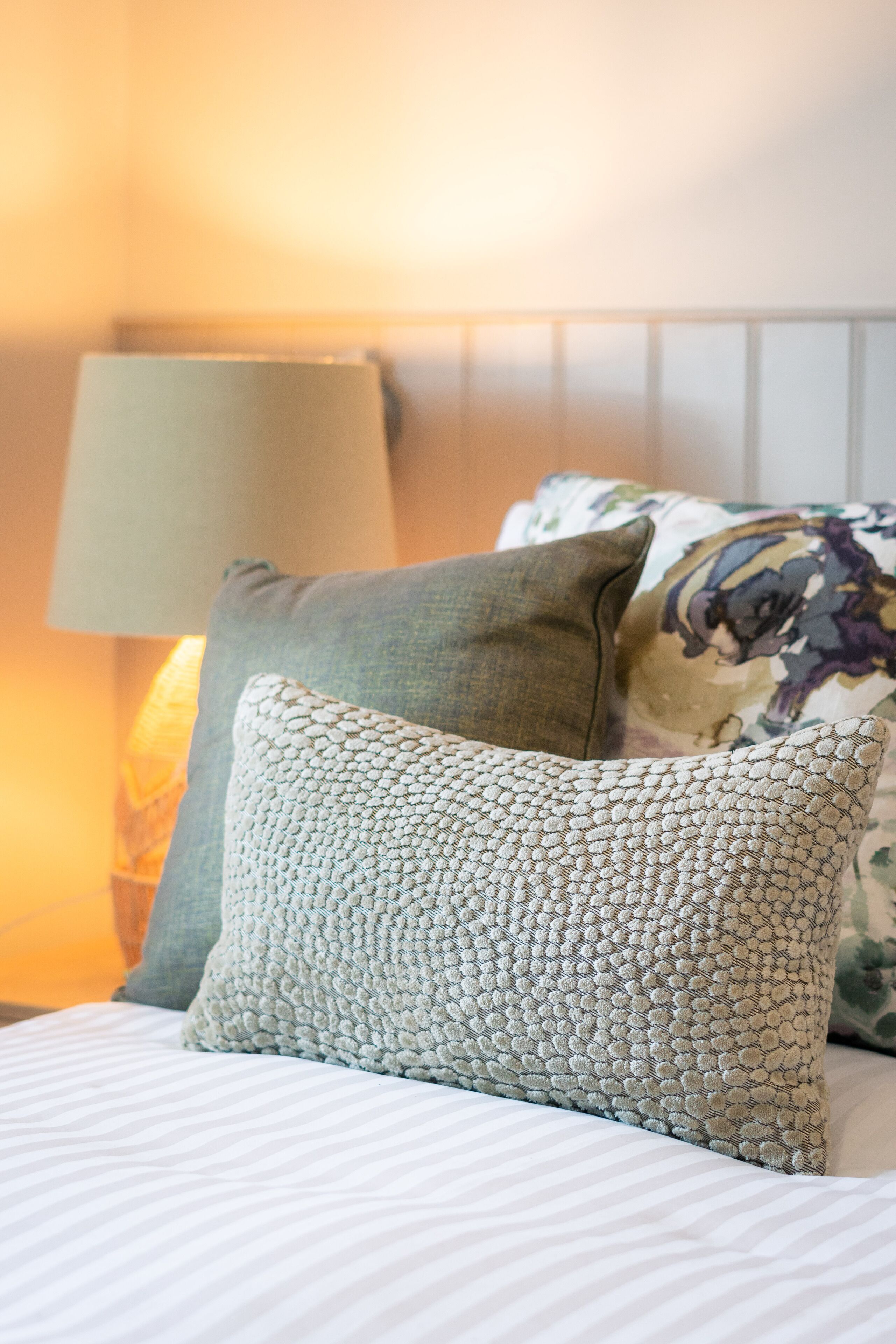 A bed with striped bedding, a green pillow, and a patterned pillow.