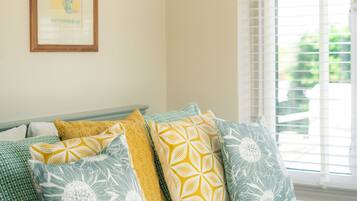A bedroom with a bed, pillows, a framed picture on the wall, and a window with blinds.