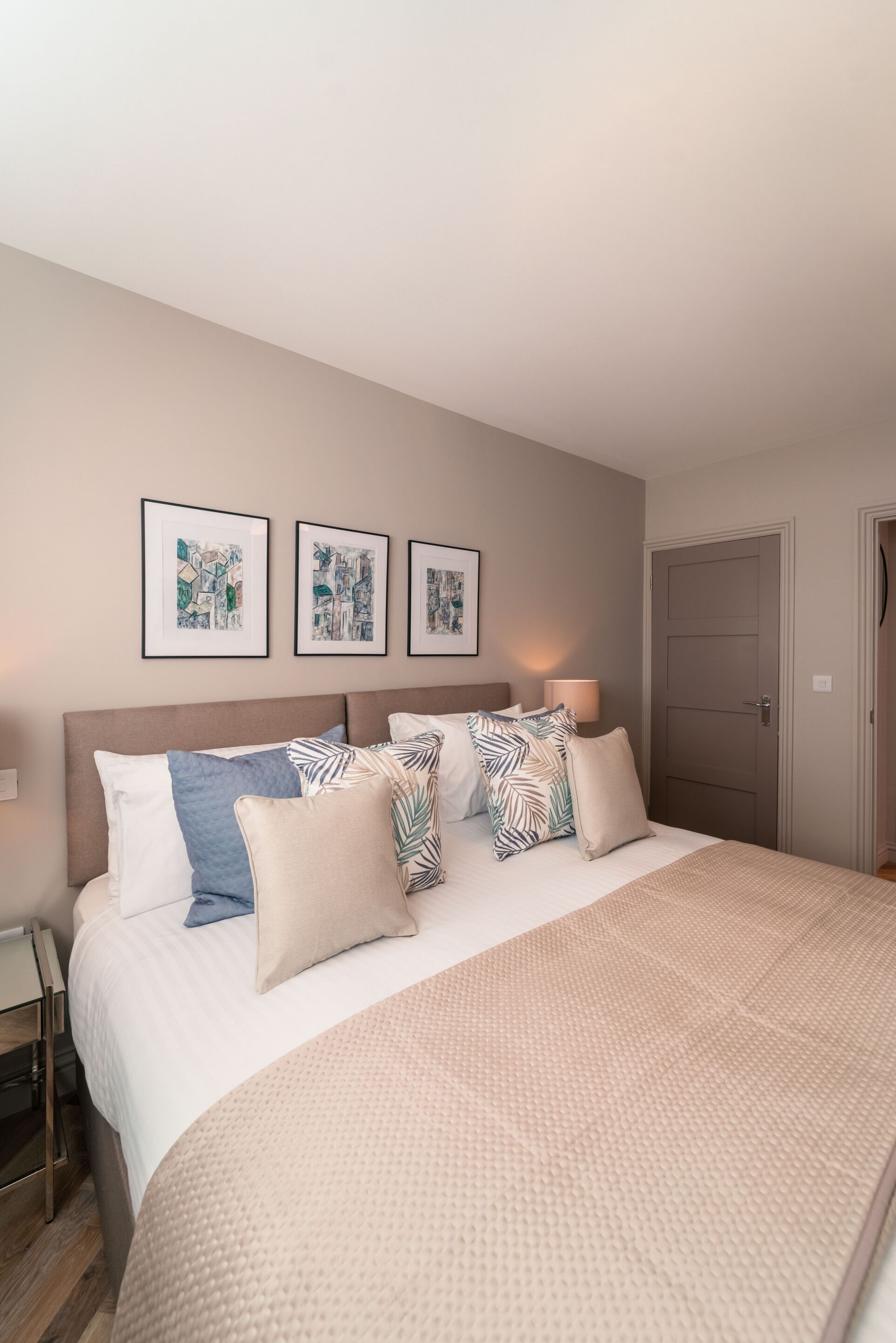 Un letto rifatto con un copriletto color beige, diversi cuscini e un quadro appeso al muro.