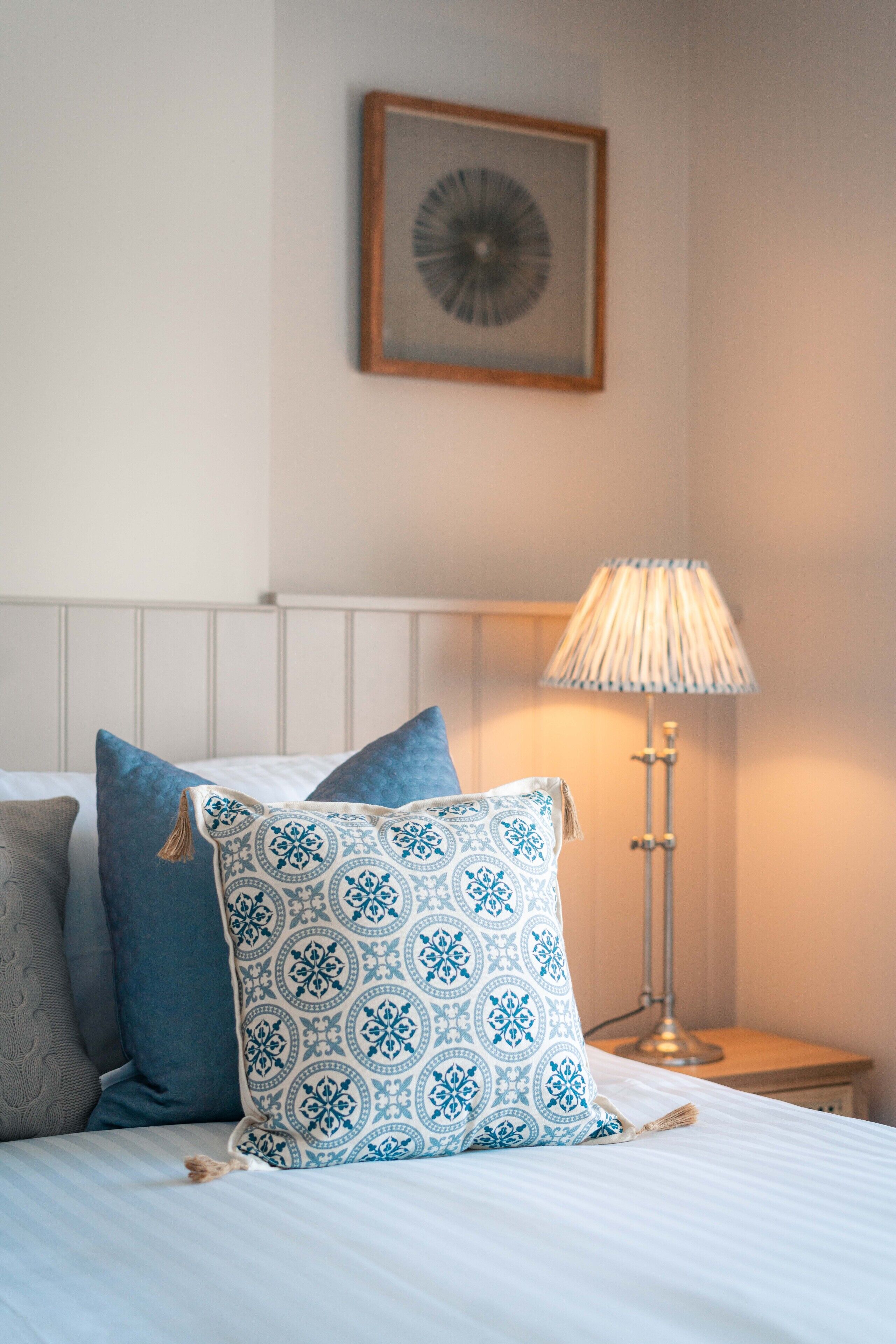 A neatly made bed with patterned pillows, a bedside lamp, and a framed picture on the wall.