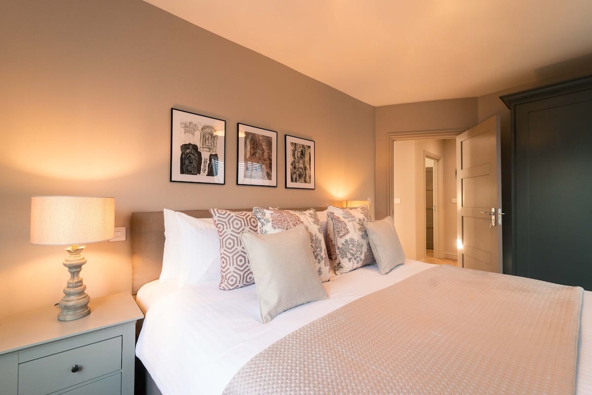 A neatly made bed with patterned pillows, a bedside lamp, and framed artwork on the wall.