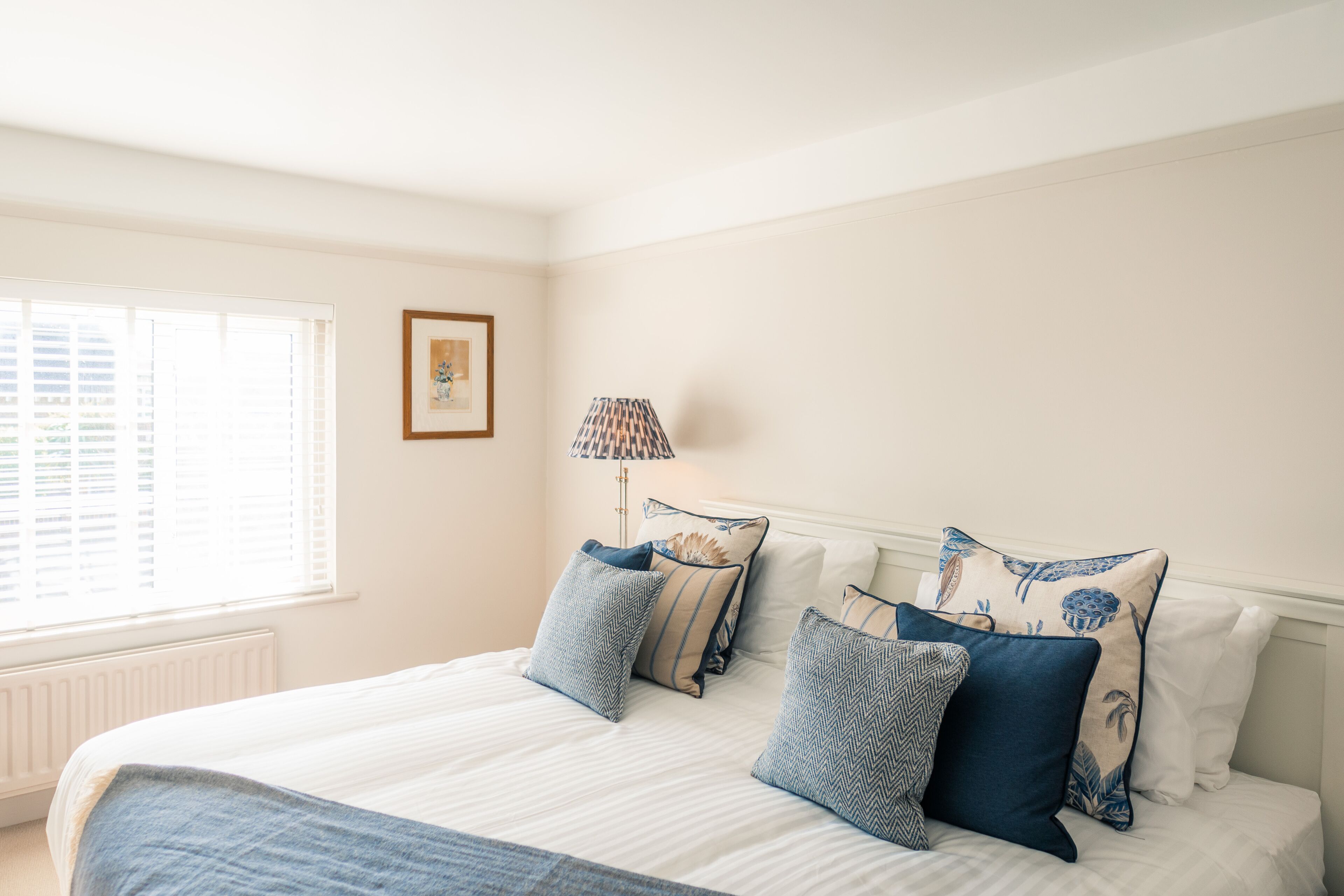 A bedroom with a large bed, a bedside table, a lamp, and a window with blinds.