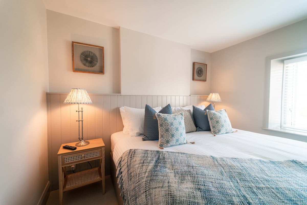 A neatly arranged bedroom with a bed, two bedside lamps, a small table, and two wall-mounted picture frames.