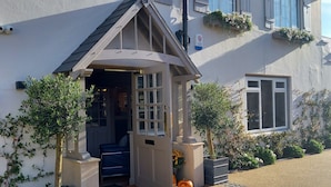 A building with a covered entrance, potted plants, and a gravel driveway.