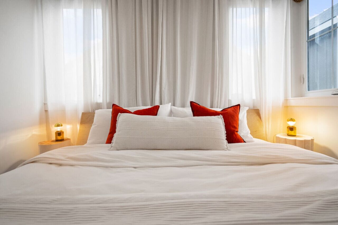 A neatly made bed with white and red pillows, a white duvet, and two bedside lamps on a nightstand.