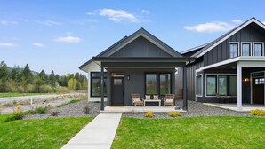 A modern two-story house with a covered porch, large windows, and a well-maintained lawn. - ✨ Modern Retreat Near Schweitzer–Hot Tub, Fireplace, 3 King Beds ✨ (Ponderay)