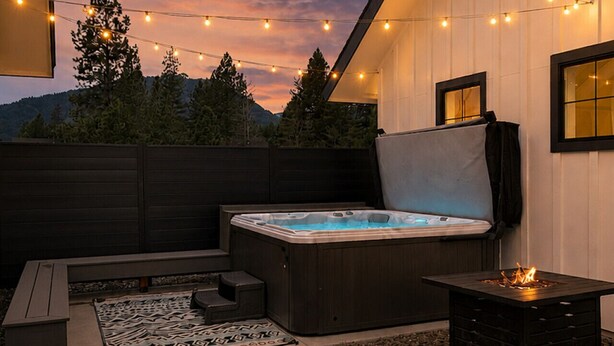 An outdoor patio with a hot tub, string lights, and a fire pit. - ✨ Modern Retreat Near Schweitzer –Hot Tub, Fireplace, 3 King Beds ✨ (Ponderay)