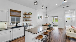 A modern kitchen with white cabinetry, a central island with stools, pendant lighting, and a ceiling fan. - ✨ Modern Retreat Near Schweitzer–Hot Tub, Fireplace, 3 King Beds ✨ (Ponderay)