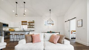 A modern living room with a white sofa, a coffee table, and a kitchen in the background. - ✨ Modern Retreat Near Schweitzer–Hot Tub, Fireplace, 3 King Beds ✨ (Ponderay)