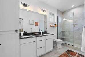 A modern bathroom with a double sink vanity, a toilet, and a glass shower enclosure.