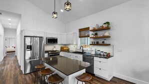 A modern kitchen with a central island, stainless steel appliances, wooden bar stools, and pendant lighting. - ✨ Modern Retreat Near Schweitzer–Hot Tub, Fireplace, 3 King Beds ✨ (Ponderay)