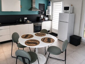 Una cucina moderna con mobili bianchi, un piano di lavoro nero e un frigorifero bianco. È presente un tavolo rotondo con quattro sedie e un tavolino con sottobicchieri.