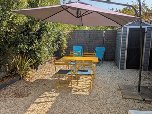 A patio with a table and chairs under a large umbrella, surrounded by gravel and plants.