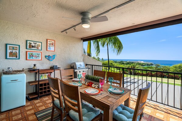Un coin repas avec une table dressée pour quatre personnes, un ventilateur de plafond et une vue sur l’océan.
