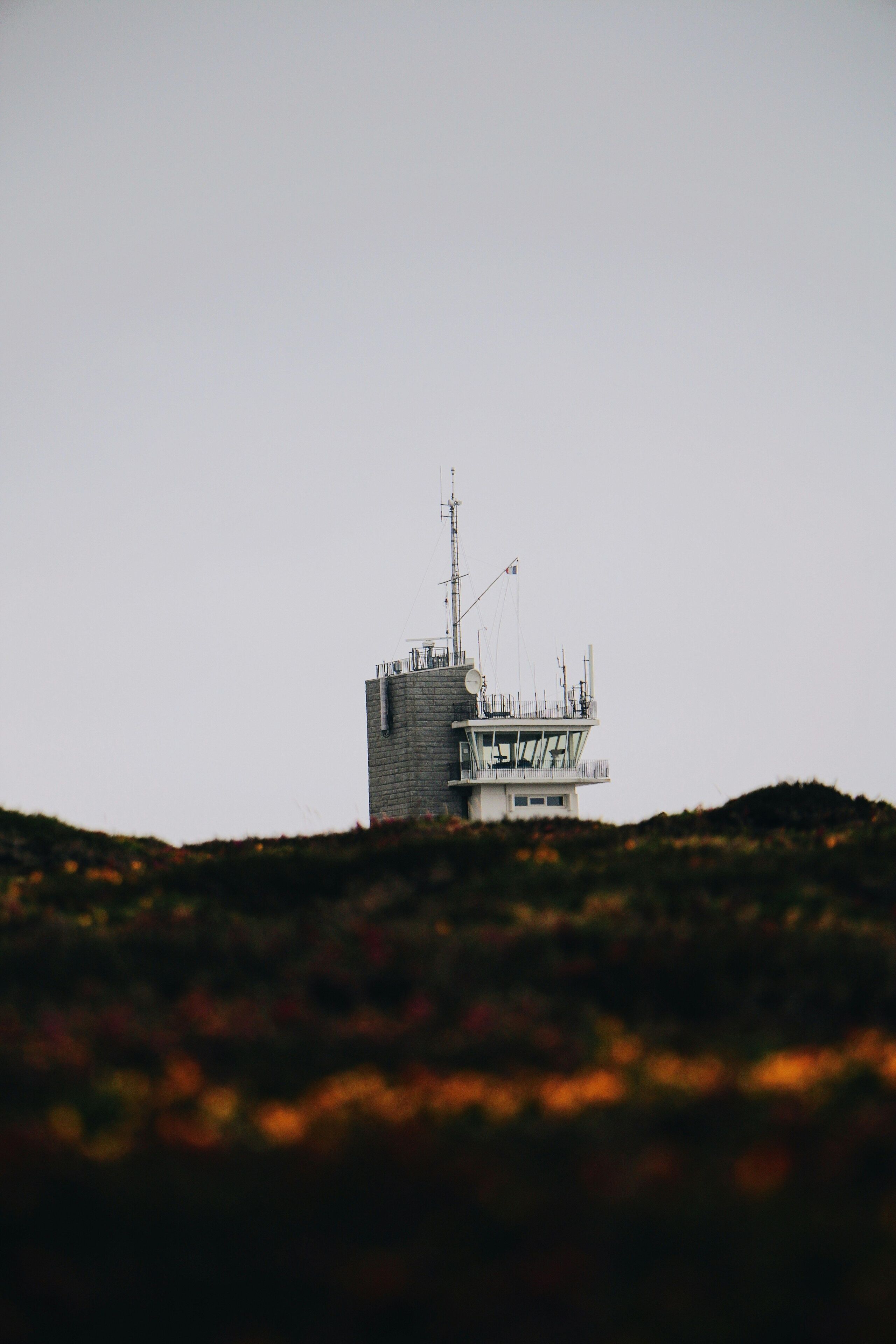 Een controle toren met een schotelantenne, omgeven door een glooiend landschap.