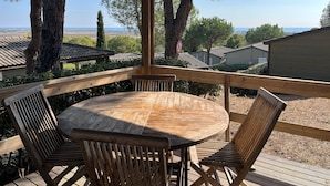 En träveranda med ett runt bord och fyra stolar, med utsikt över ett vackert landskap med träd och havet i bakgrunden.