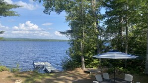 Un patio junto al lago con una mesa, sillas, un muelle y un paraguas grande.