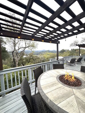 An outdoor patio with a round table, chairs, a fire pit, and a pergola with string lights.